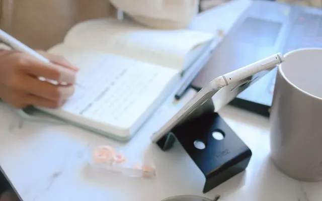 Hand writing notes beside a laptop