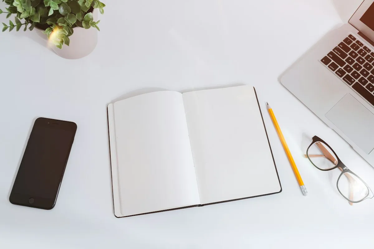 Notebook, phone and laptop on a white desk